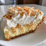 A tall slice of Coconut cream pie featuring a thick layer of creamy filling, whipped cream, and toasted coconut flakes.