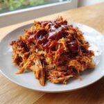 A generous serving of shredded Slow Cooker Pulled Pork topped with rich, glossy barbecue sauce on a light plate.