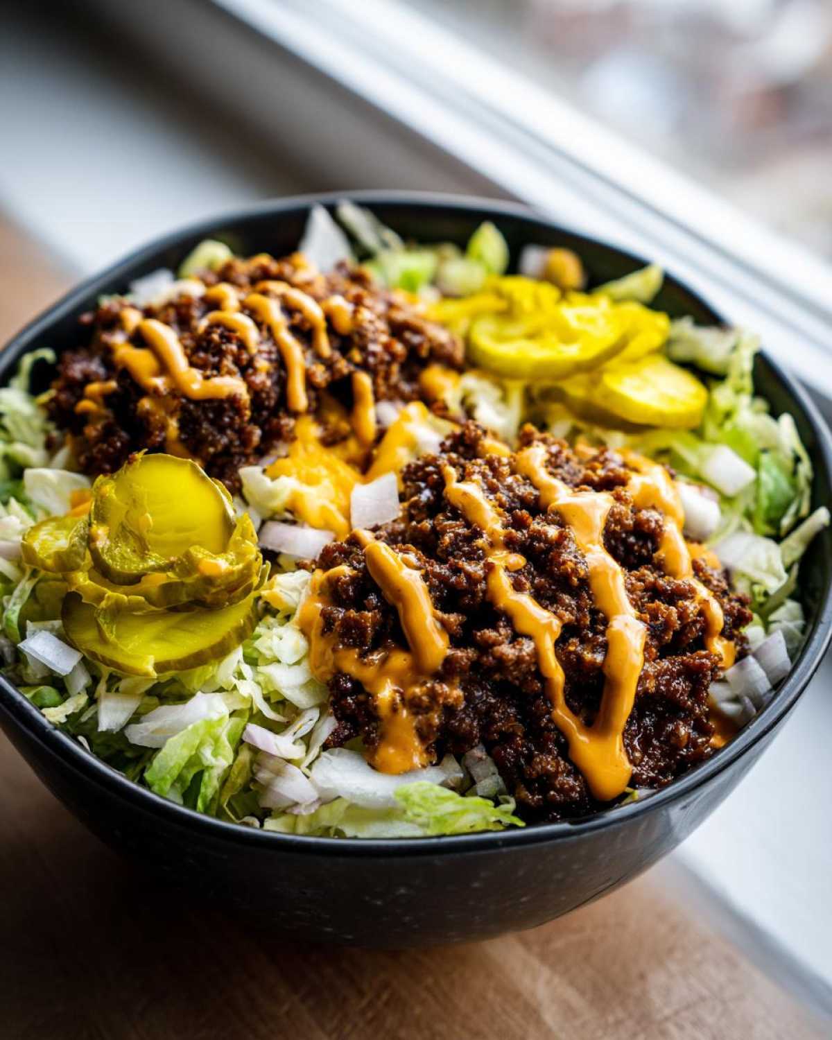 A close-up of a hearty smash burger bowl featuring seasoned ground beef, shredded lettuce, pickles, and a drizzle of orange burger sauce.