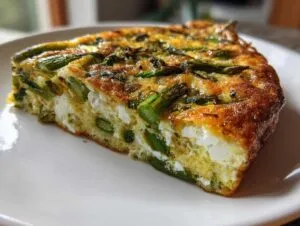 Close-up of a thick slice of Spring vegetable frittata featuring bright green asparagus and white cheese.