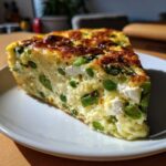 A thick slice of golden brown Spring vegetable frittata filled with bright green peas, asparagus, and white cheese.