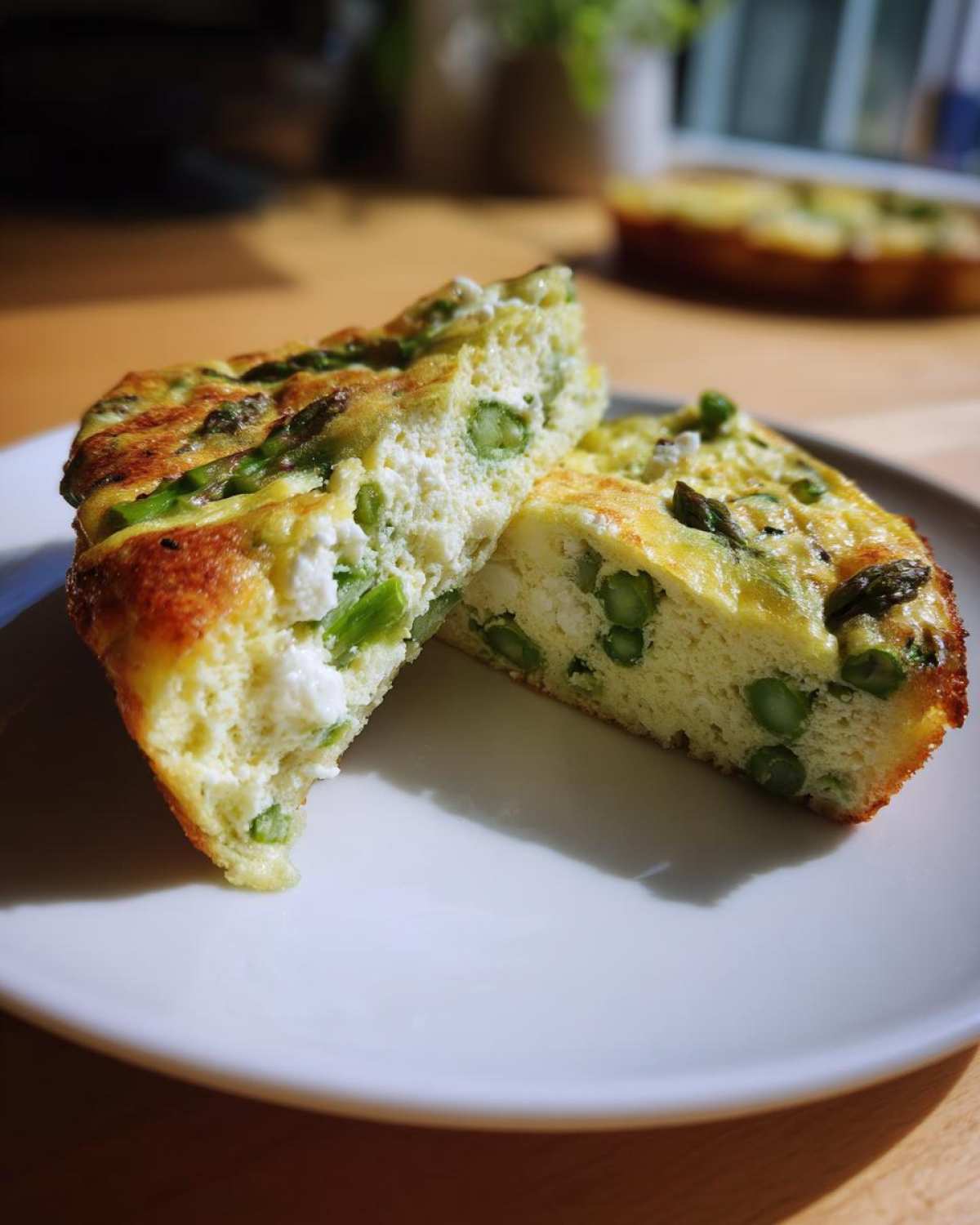 Two slices of fluffy Spring vegetable frittata featuring green asparagus and white cheese on a white plate.